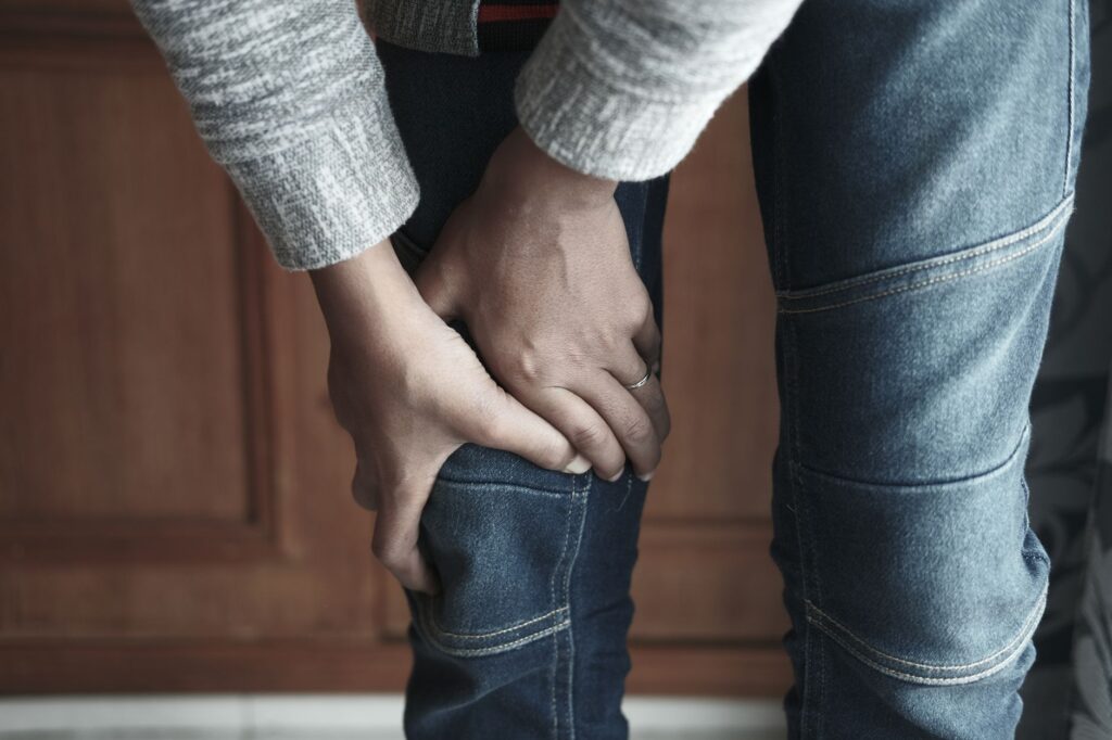 A person holds their knee in denim jeans, showing a sense of tension, what sciatica pain actually feels like