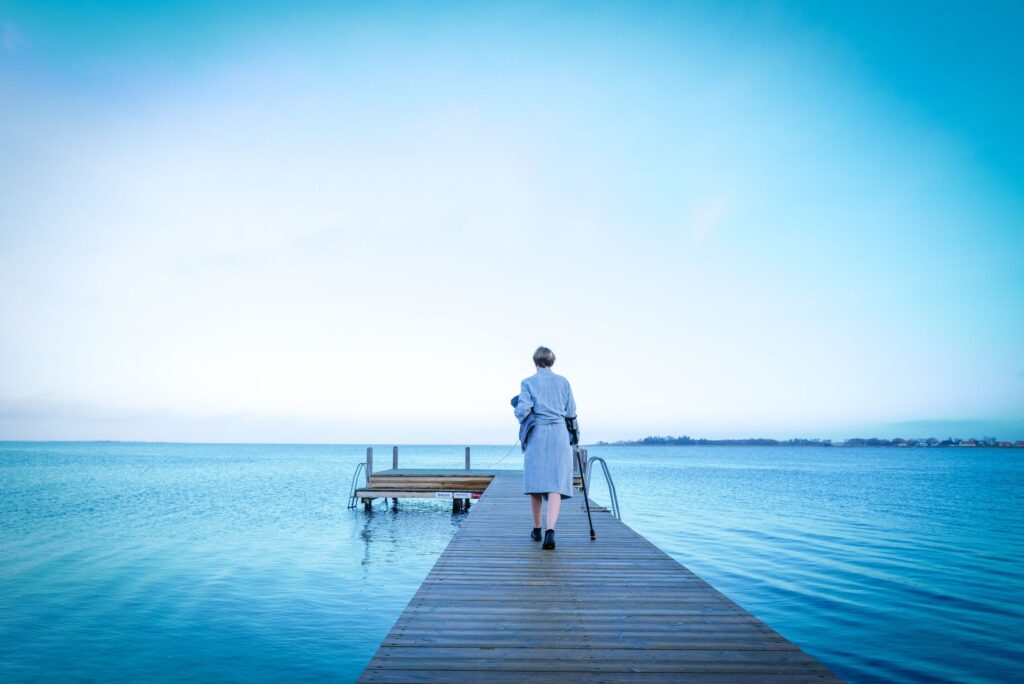 A serene scene of a woman in a coat walking down a wooden pier towards the sea.